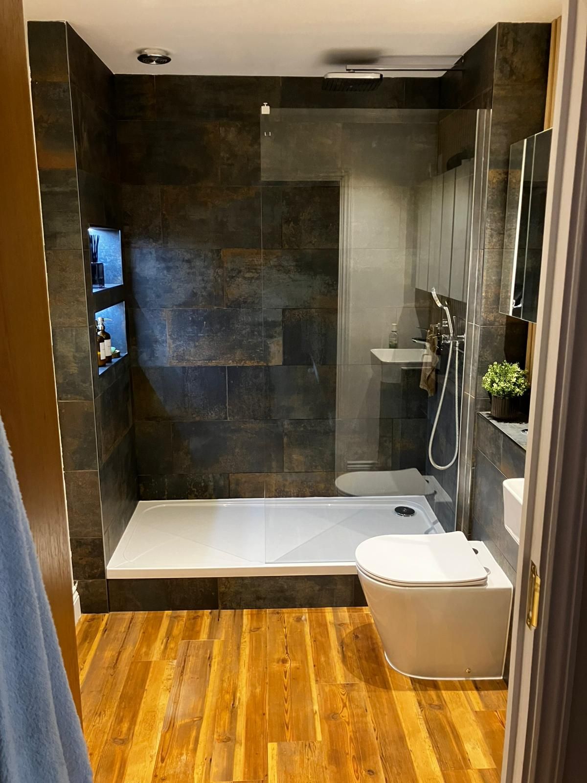 Walk-in shower with dark tiles and wood floor